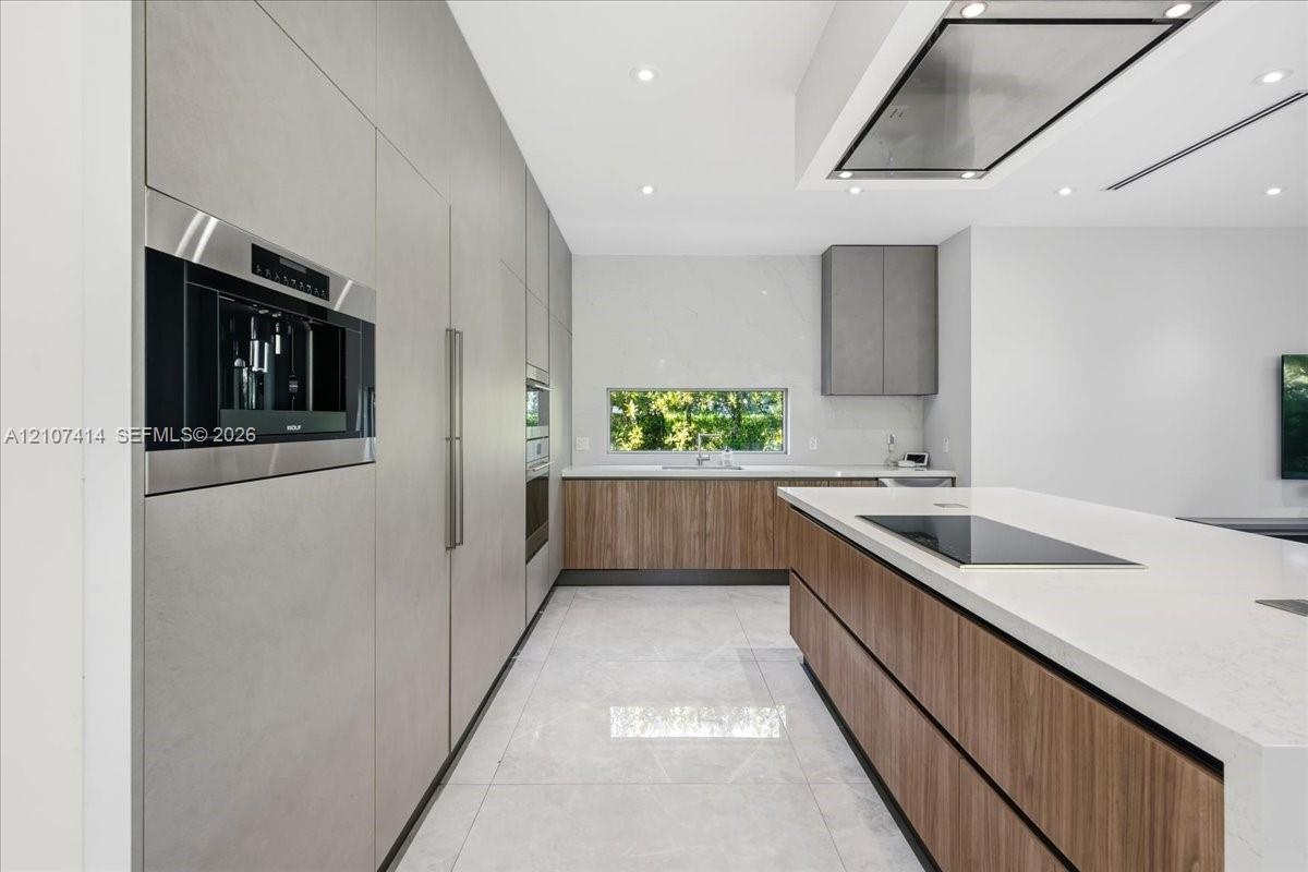 Modern kitchen featuring custom wood-finish cabinetry, waterfall-edge stone countertops, integrated stainless steel appliances, a flush-mount cooktop,
