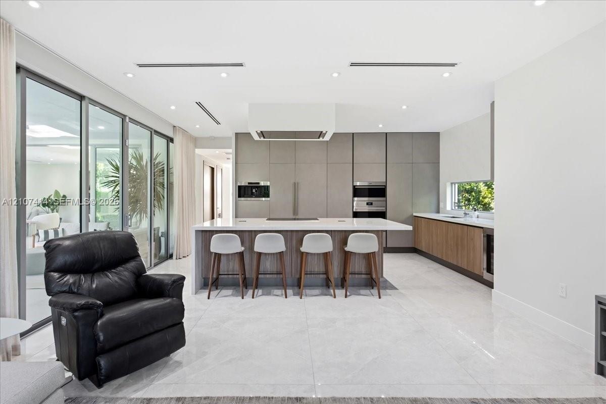 Chef’s kitchen featuring full-height matte cabinetry, a waterfall-edge stone island, built-in stainless steel appliances, polished stone flooring, and
