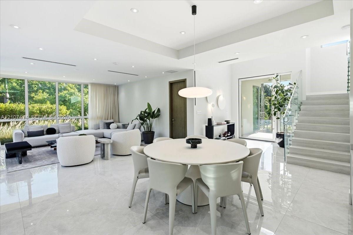 Open-concept interior featuring large-format polished stone flooring, tray ceilings with recessed lighting, floor-to-ceiling windows, and a staircase 