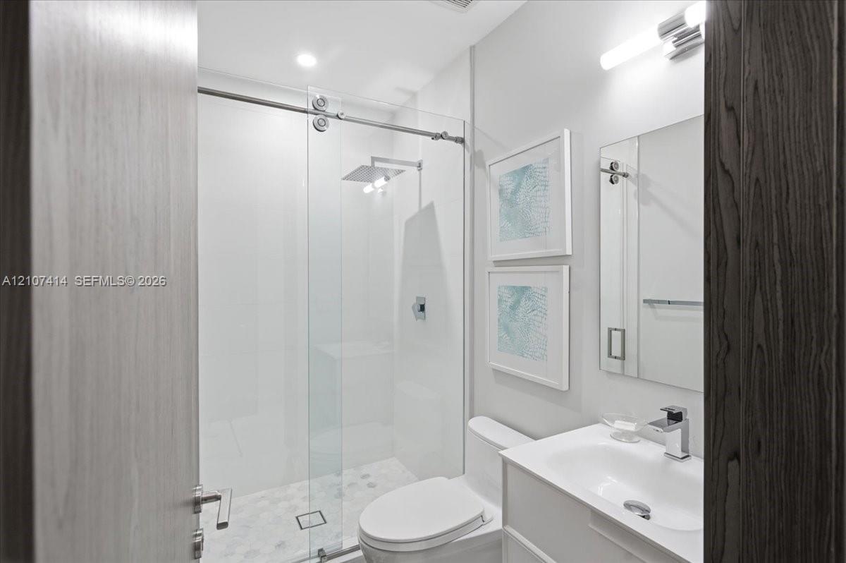 Walk-in shower with sliding glass enclosure and rainfall showerhead, white vanity with integrated basin, polished chrome fixtures, and wall-mounted va