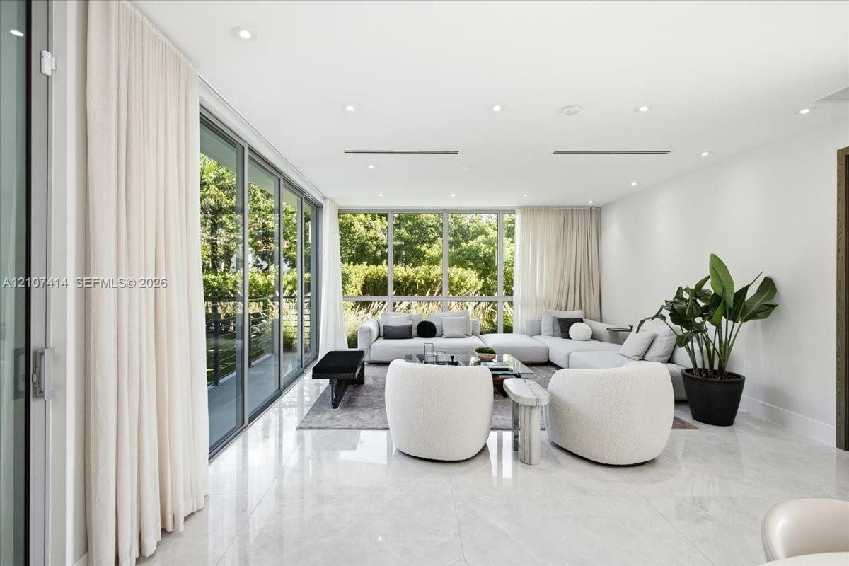 Open-concept interior featuring large-format polished stone flooring, floor-to-ceiling glass sliding doors, expansive glass windows, and recessed ligh