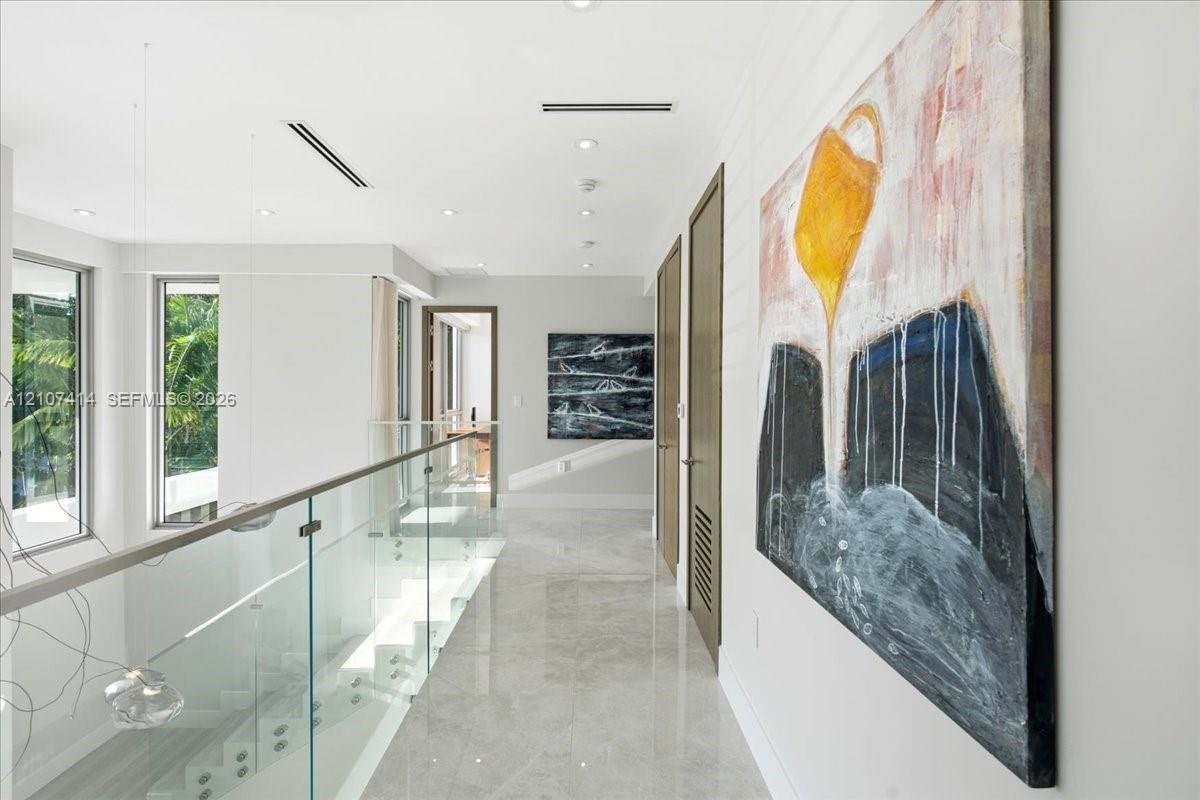 Hallway featuring polished tile flooring, a glass panel railing with metallic hardware, recessed ceiling lighting, and solid wood-finish doors