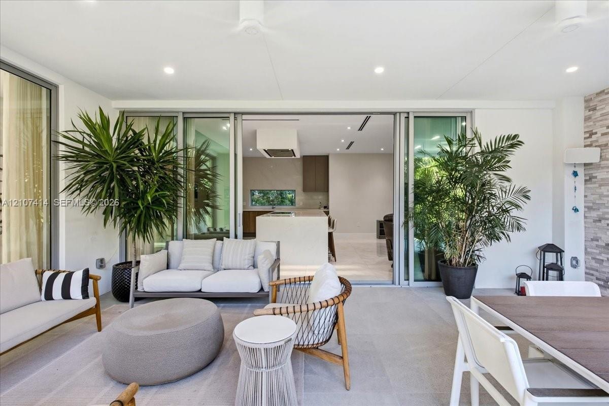 Covered patio featuring large-format stone-finish flooring, recessed ceiling lighting, and expansive floor-to-ceiling multi-panel sliding glass doors 