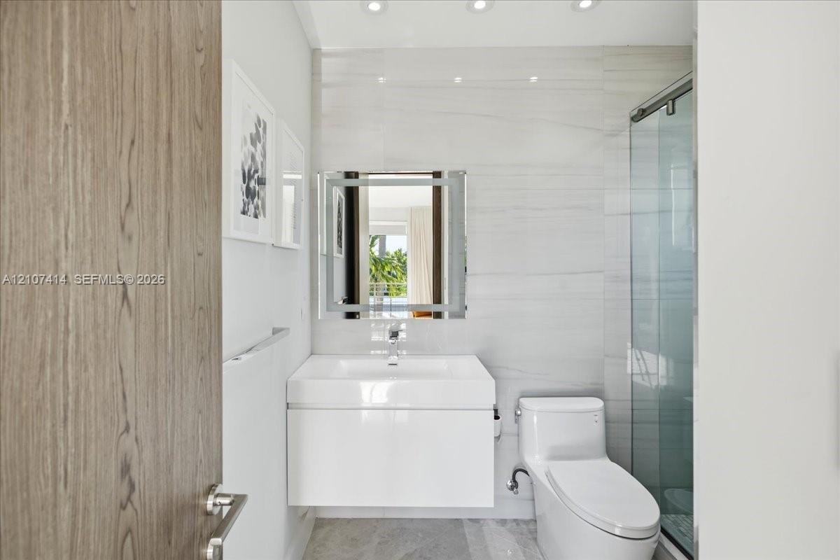 Modern bathroom featuring a white floating vanity with a vessel sink, integrated LED-lit mirror, glass-enclosed shower, and stone-finish floor tiling