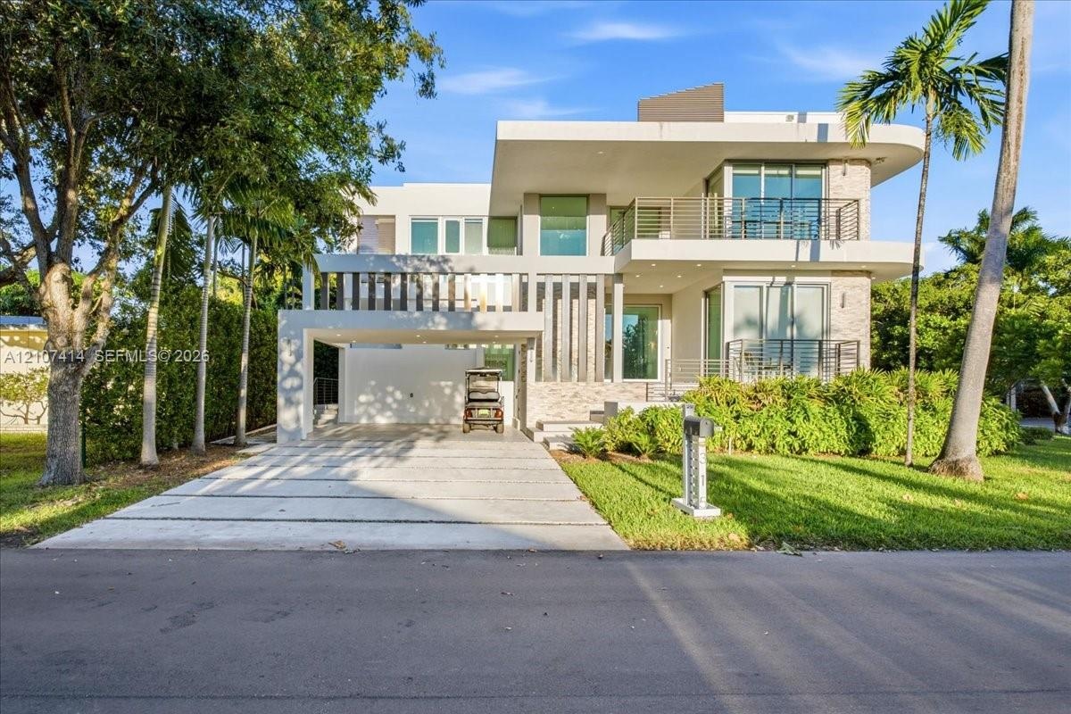 Modern three-story architecture featuring stone masonry accents, a covered parking structure, metal balcony railings, and expansive glass window panel