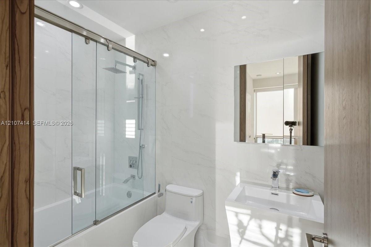 Bathroom featuring full-height stone-finish wall tile, a glass-enclosed shower with a rainfall showerhead, a wall-mounted medicine cabinet, and a cont