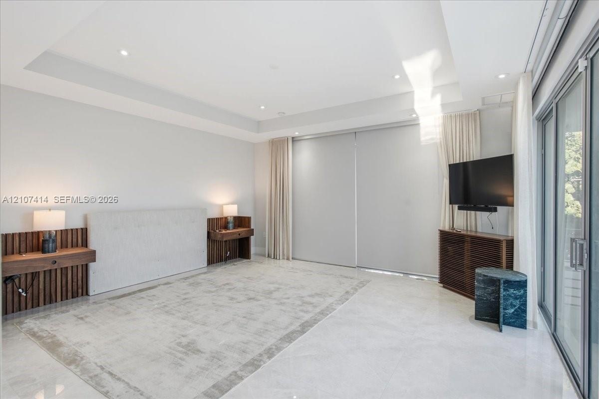 Tray ceiling with recessed lighting, integrated wood-slat wall paneling, built-in wooden shelving, oversized tile flooring, and floor-to-ceiling slidi