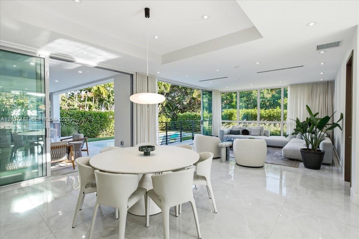Open-concept living space featuring large-format tile flooring, recessed lighting, a tray ceiling, and floor-to-ceiling glass sliding doors providing 