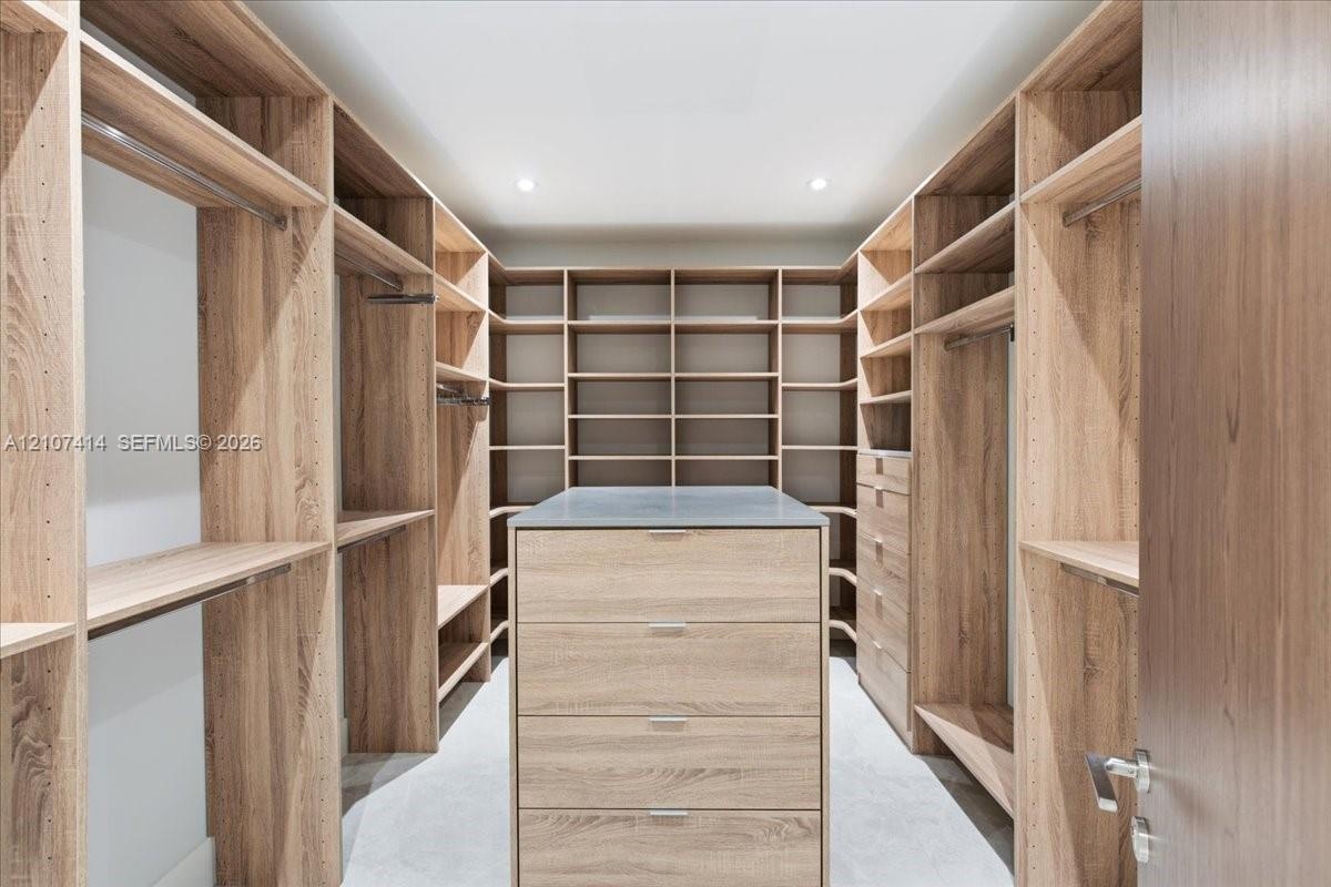 Custom walk-in closet featuring extensive wood-finish built-in shelving, hanging rods, an integrated center island with drawers, and a solid counterto