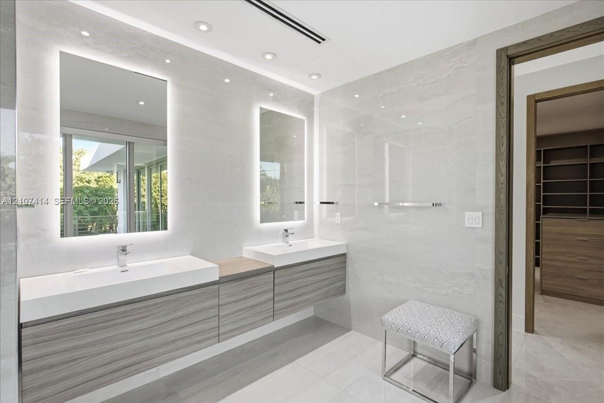 Floating double vanity with wood-finish cabinetry, integrated rectangular sinks, polished chrome fixtures, back-lit vanity mirrors, and floor-to-ceili
