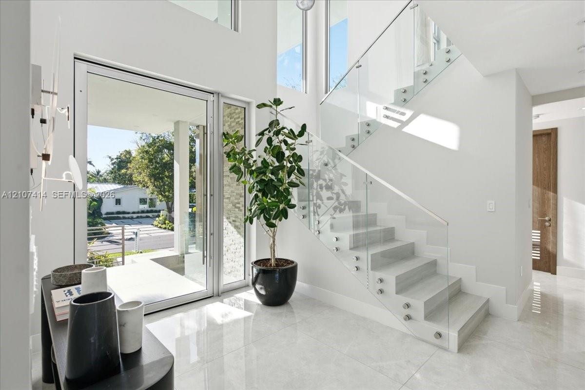 Entryway featuring polished stone flooring, a multi-story ceiling, floor-to-ceiling windows, and a floating staircase with glass panel railings