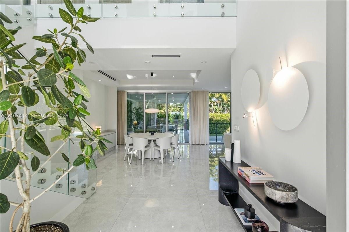 Double-height entryway featuring polished tile flooring, glass-panel staircase railing, recessed lighting, and wall-mounted circular accent fixtures