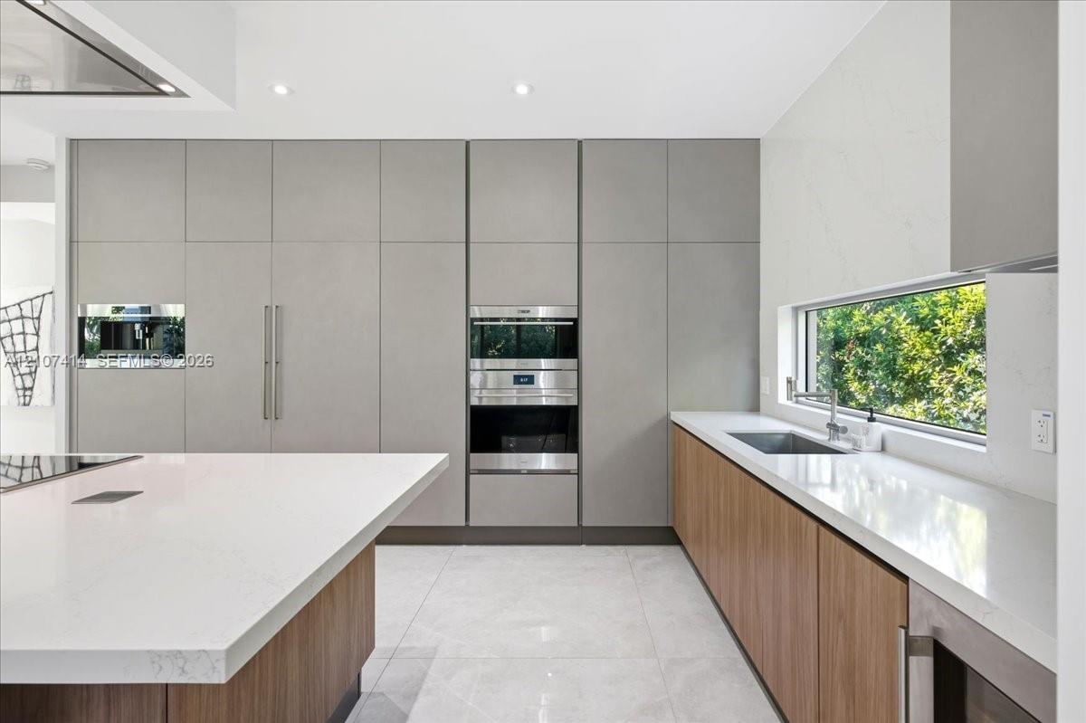 Modern kitchen featuring floor-to-ceiling flat-panel cabinetry, a large central island with white quartz countertops, integrated stainless steel appli