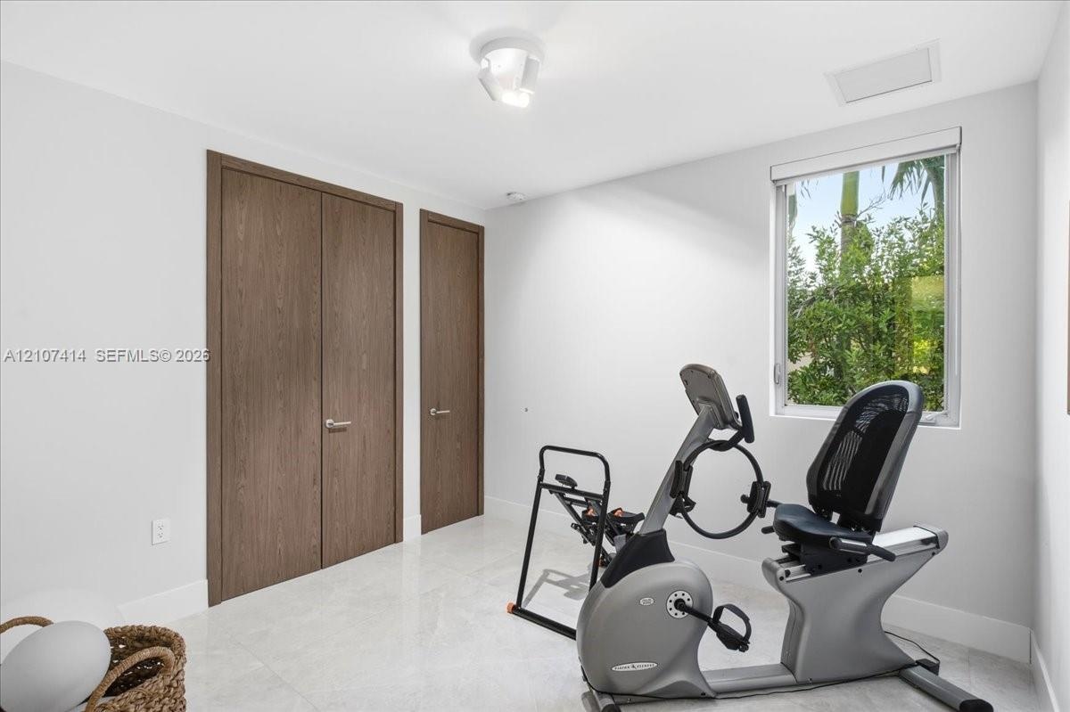 Neutral-toned interior space featuring light-colored stone-finish flooring, solid wood-finish doors with metallic hardware, and a single-pane window w
