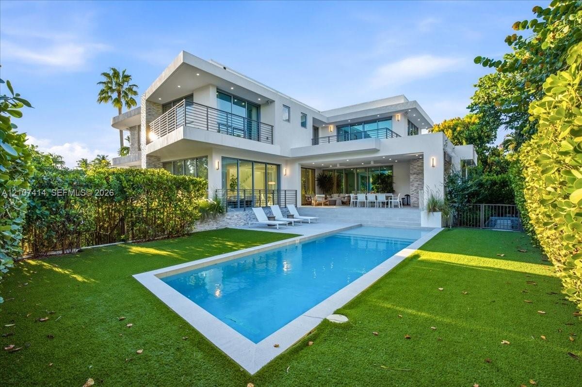 Modern two-story exterior featuring smooth stucco finish, stone accent pillars, expansive glass sliding doors, elevated balconies with metal railings,
