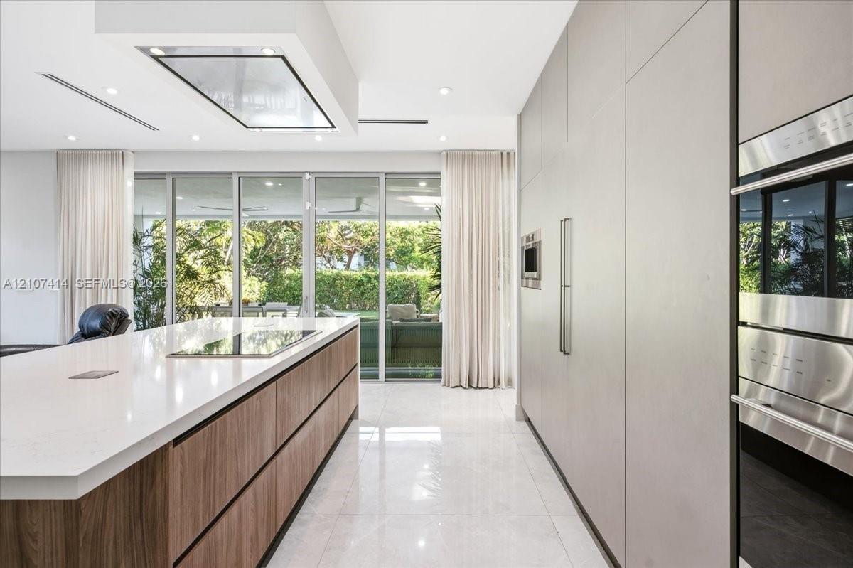Contemporary kitchen featuring a large island with wood-finish cabinetry, a waterfall-edge stone countertop, integrated flush-panel cabinetry, stainle
