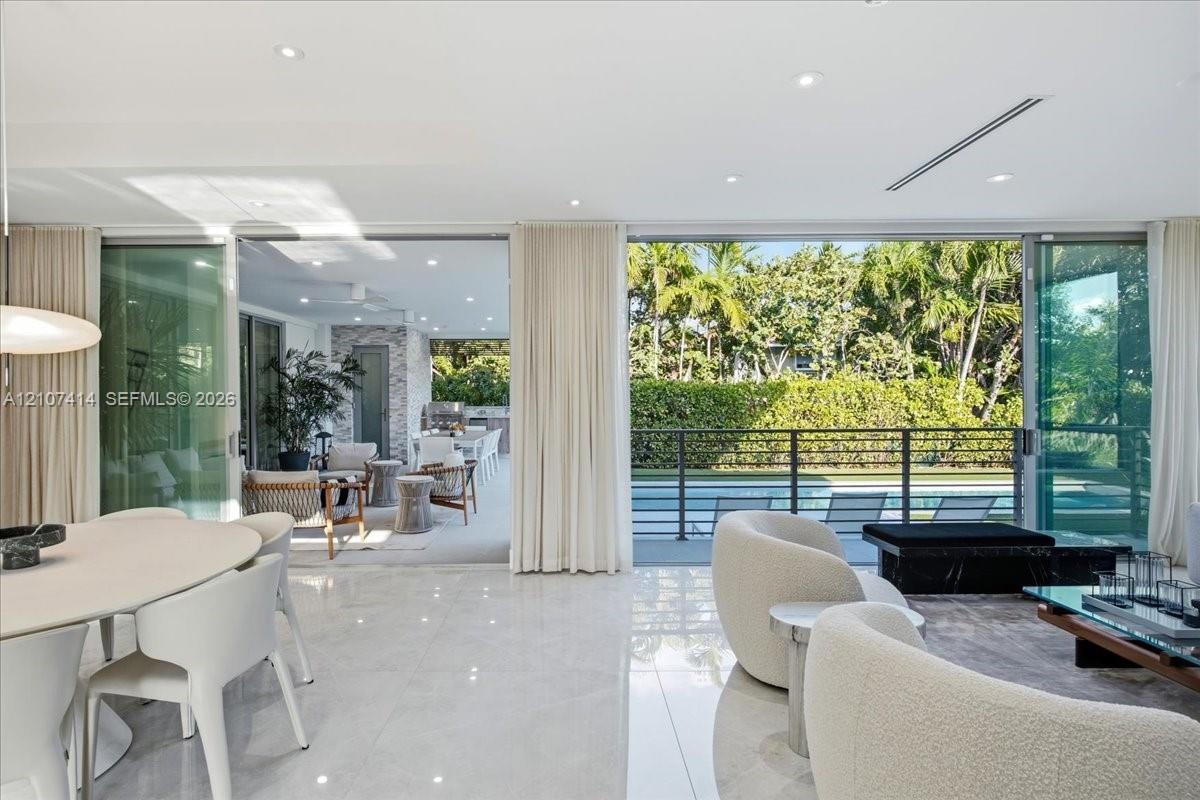 Open-concept interior featuring large-format stone flooring, floor-to-ceiling glass sliding doors, recessed lighting, and a covered outdoor patio