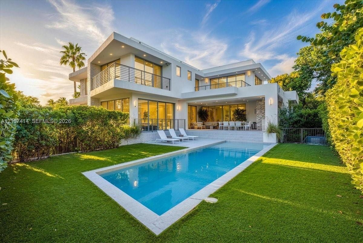 Modern two-story architectural exterior featuring expansive glass sliding doors, multiple balconies with metal railings, a rectangular swimming pool, 