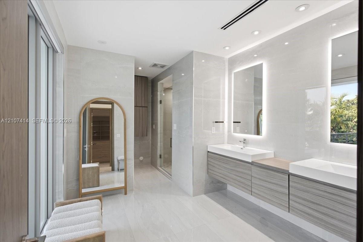 Dual floating vanity with horizontal wood-finish cabinetry, integrated rectangular sinks, and backlit mirrors, accented by large-format neutral wall t