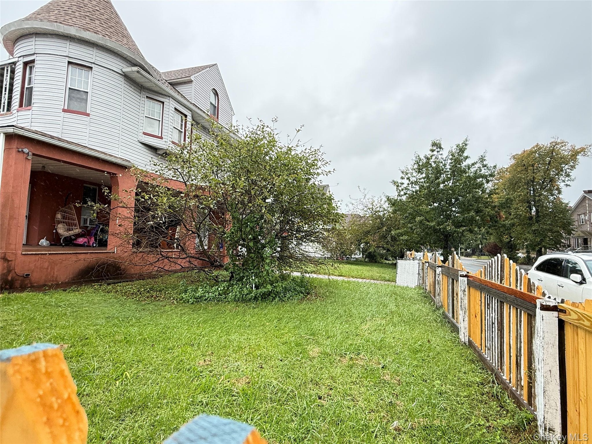 Exterior featuring a covered porch with masonry pillars, a turret architectural element, and a wooden picket fence