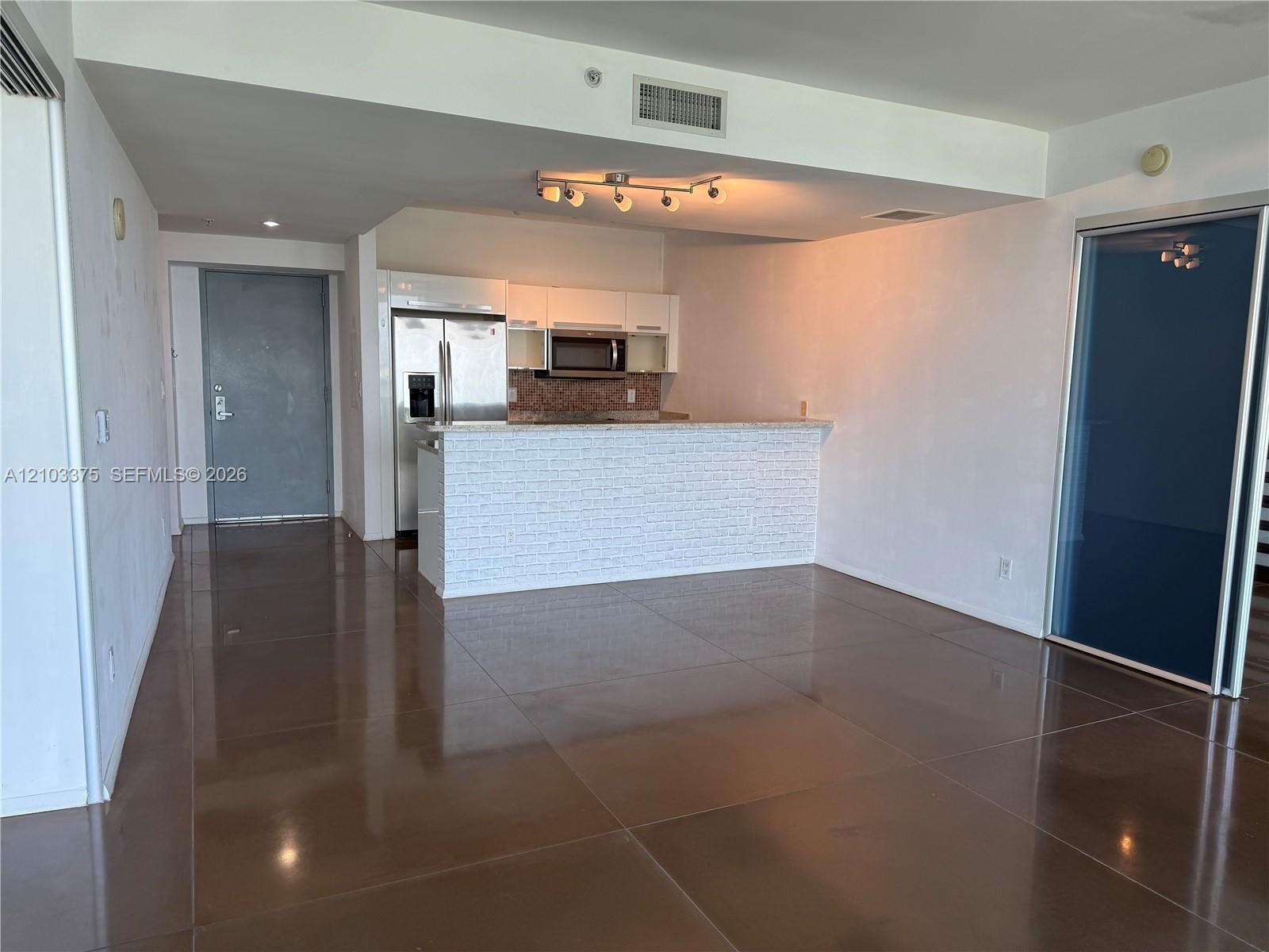 Kitchen featuring a breakfast bar with textured stone-style cladding, high-gloss white cabinetry, stainless steel appliances, and large-format tile fl