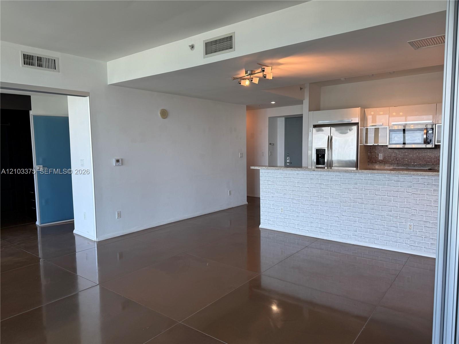 Open concept living area featuring large-format tile flooring, a kitchen breakfast bar with brick-style siding, stainless steel appliances, and multi-