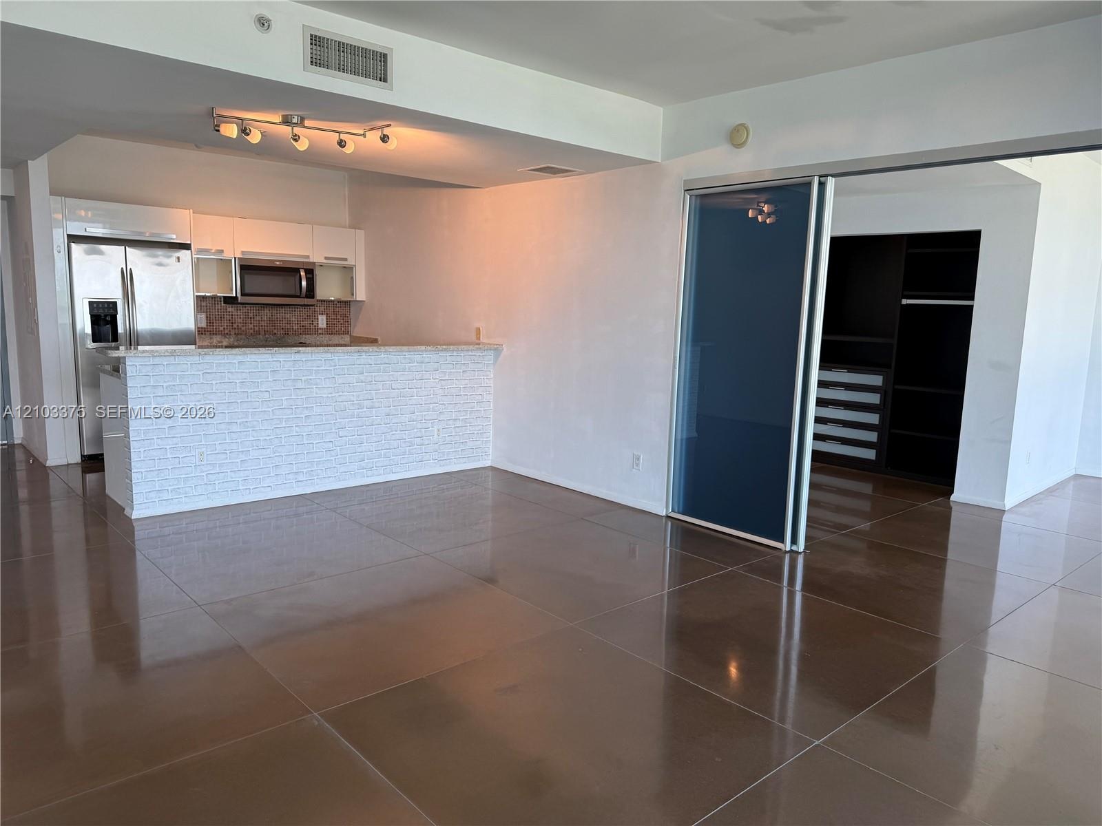 Kitchen featuring white cabinetry, stainless steel appliances, a breakfast bar with textured stone-style cladding, large-format tile flooring, and a s