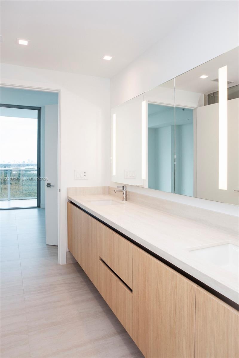 Floating vanity featuring a wood-finish cabinet, dual undermount sinks, stone-finish countertop, full-width mirror with integrated vertical lighting, 