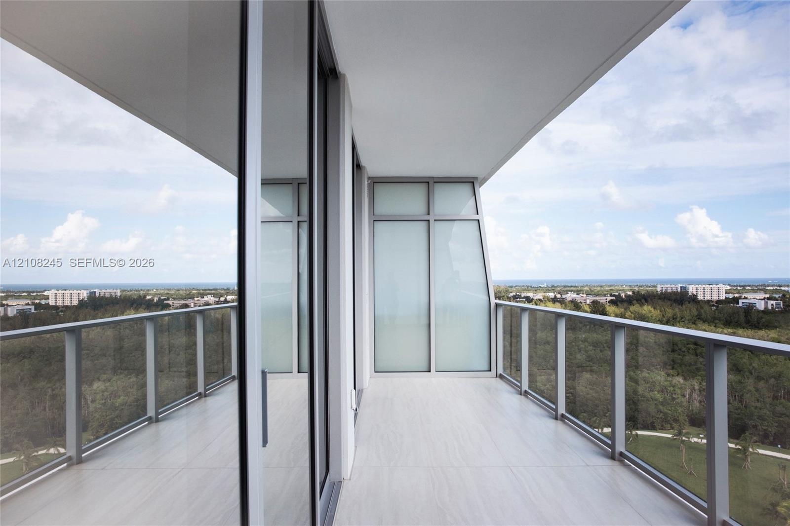 Covered balcony featuring expansive glass panel railings, floor-to-ceiling sliding glass doors, and tiled flooring