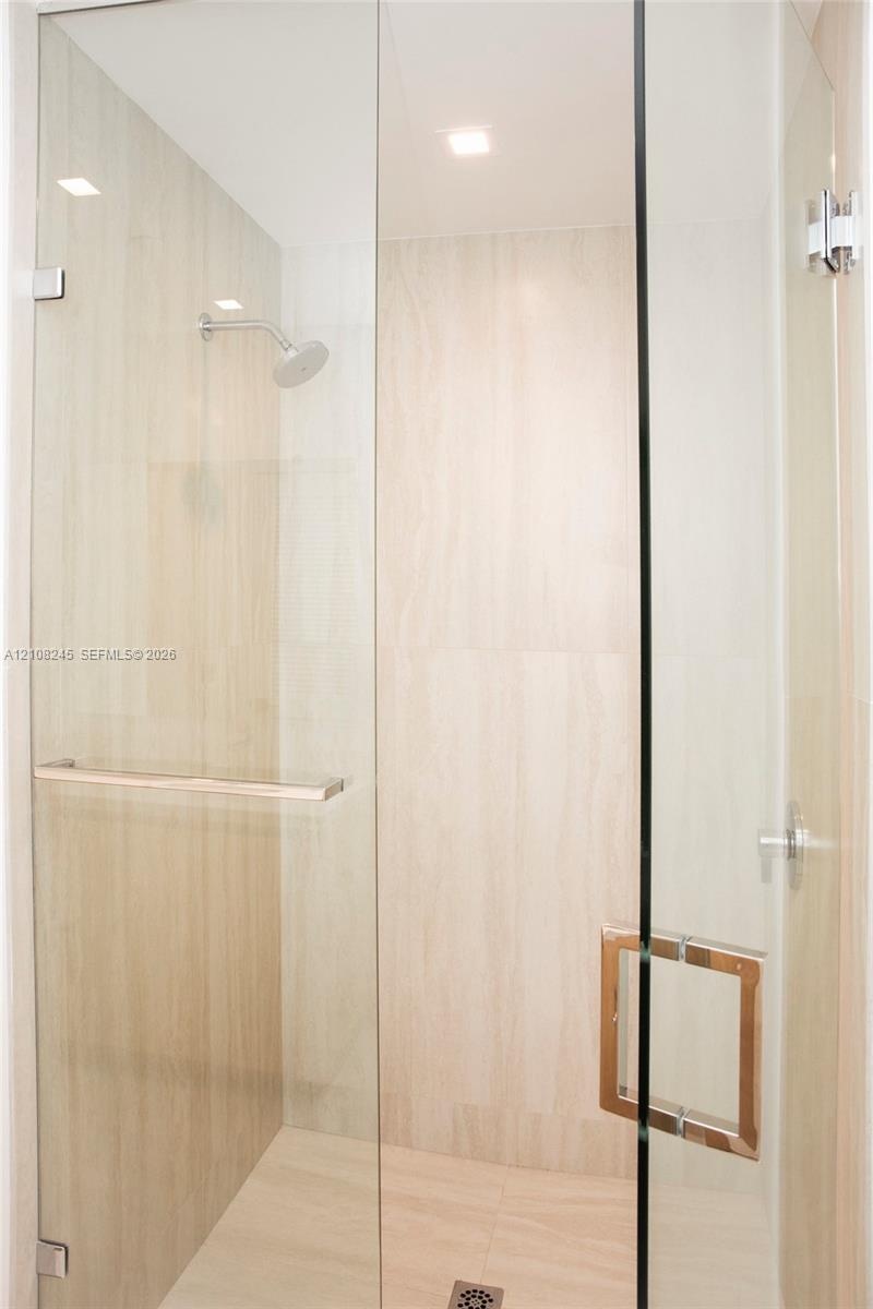 Walk-in shower enclosure featuring floor-to-ceiling neutral stone-finish tile, frameless glass paneling, polished chrome hardware, and an integrated w