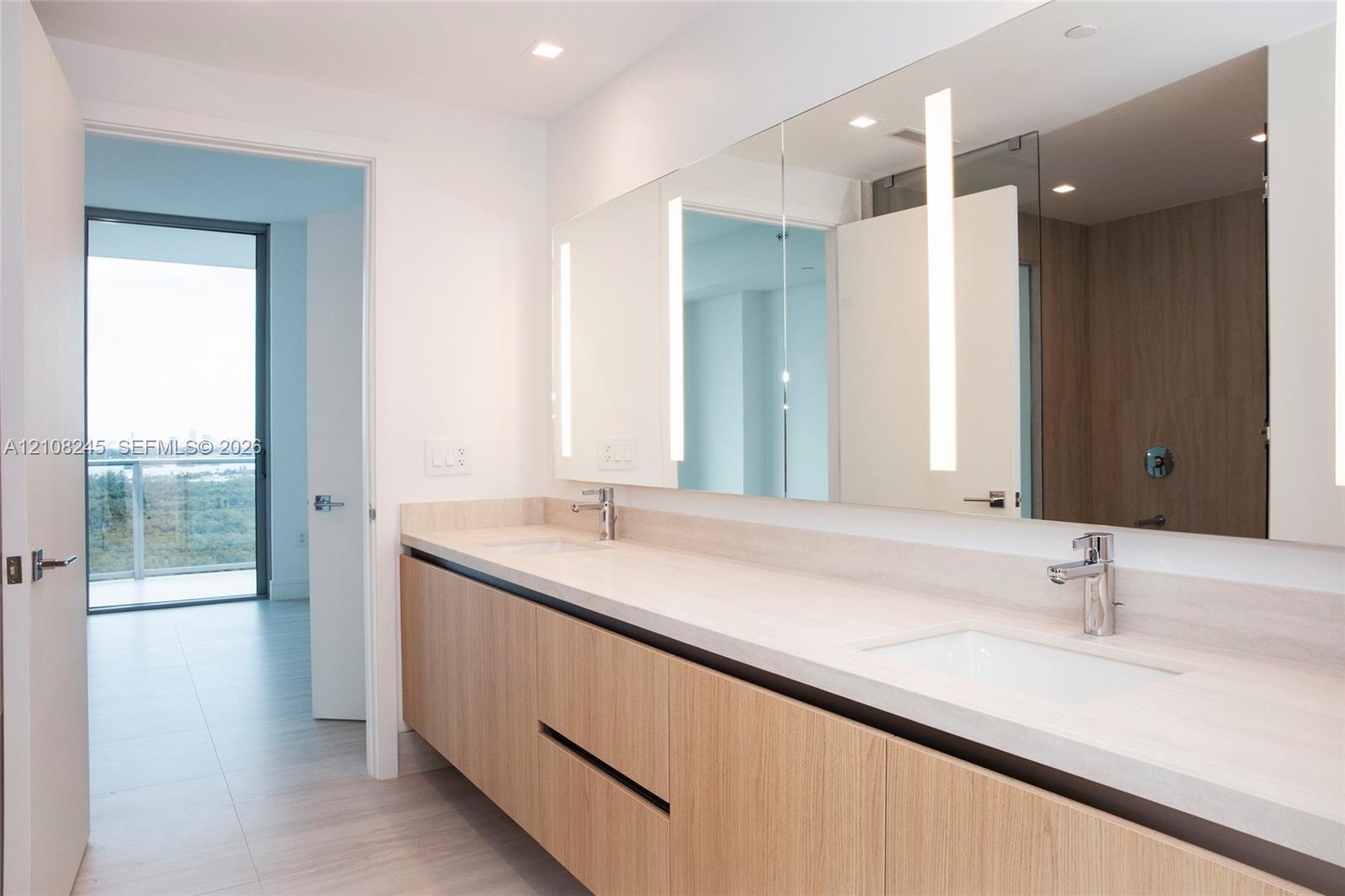 Floating vanity with wood-finish cabinetry, dual undermount sinks, light-toned stone countertop, integrated vertical LED mirror lighting, and polished