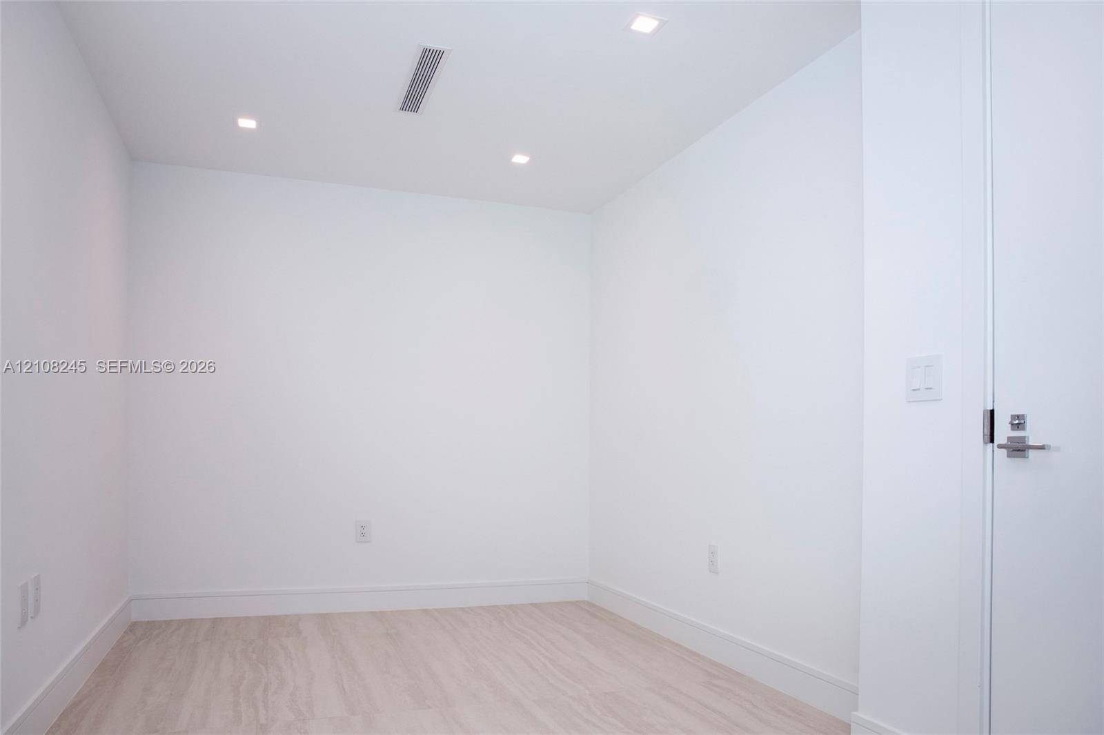 Minimalist interior featuring white wall finishes, wood-finish flooring, and recessed ceiling lighting