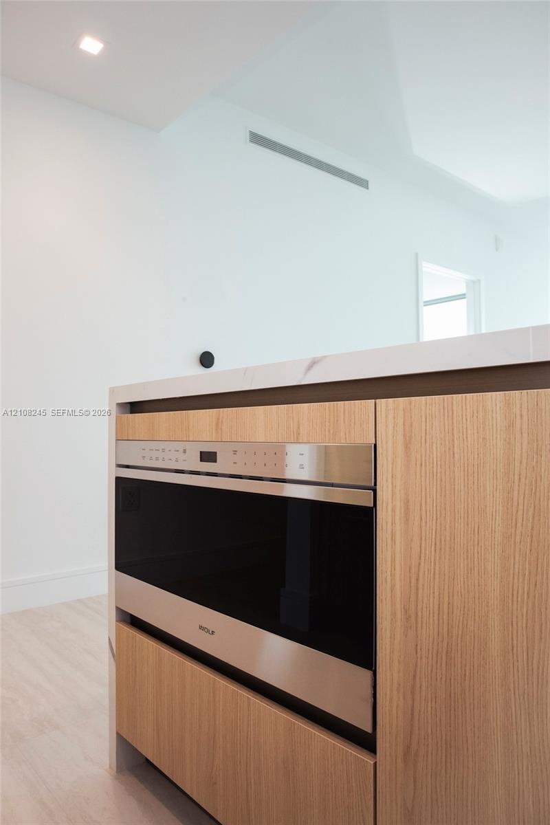 Kitchen island featuring wood-finish cabinetry, integrated stainless steel microwave drawer, and stone countertop with waterfall edge