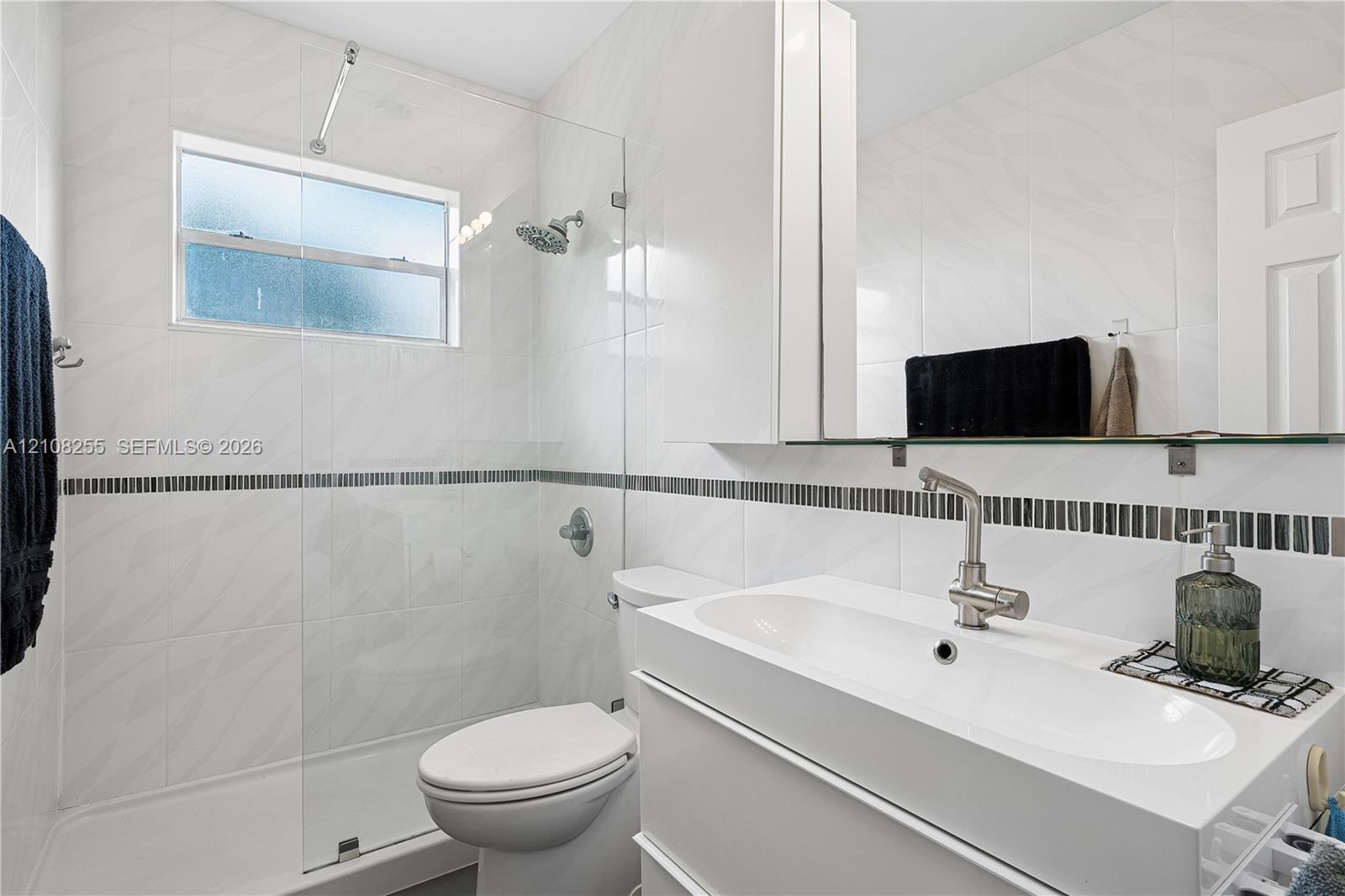 Bathroom featuring white wall tile with a mosaic accent border, a glass-enclosed shower, a floating vanity with an integrated sink, and brushed-nickel