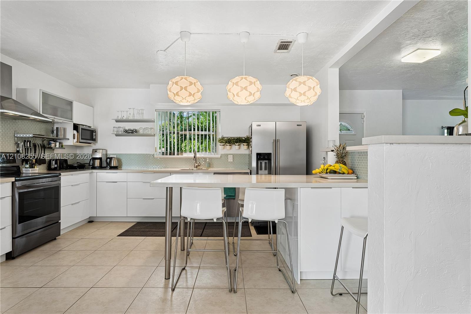 Kitchen featuring flat-panel white cabinetry, stainless steel appliances, quartz countertops, a tile backsplash, and three suspended geometric pendant