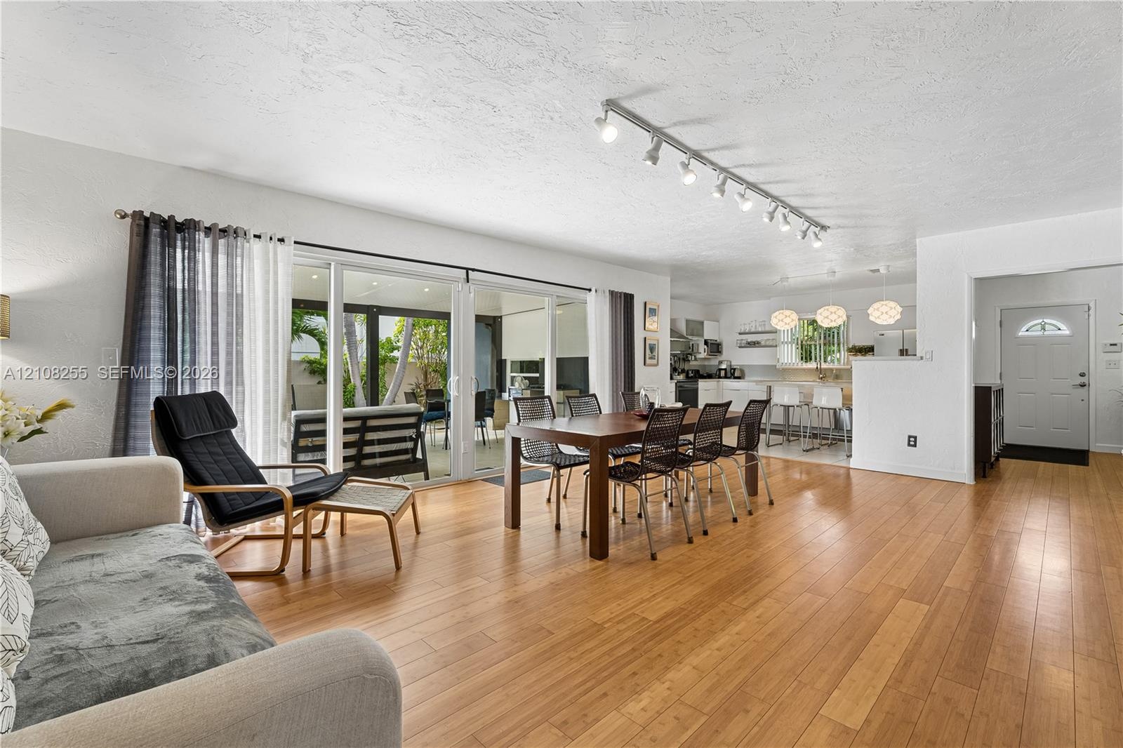 Open-concept interior with wood-finish flooring, sliding glass doors, adjustable track lighting, and a six-panel entry door