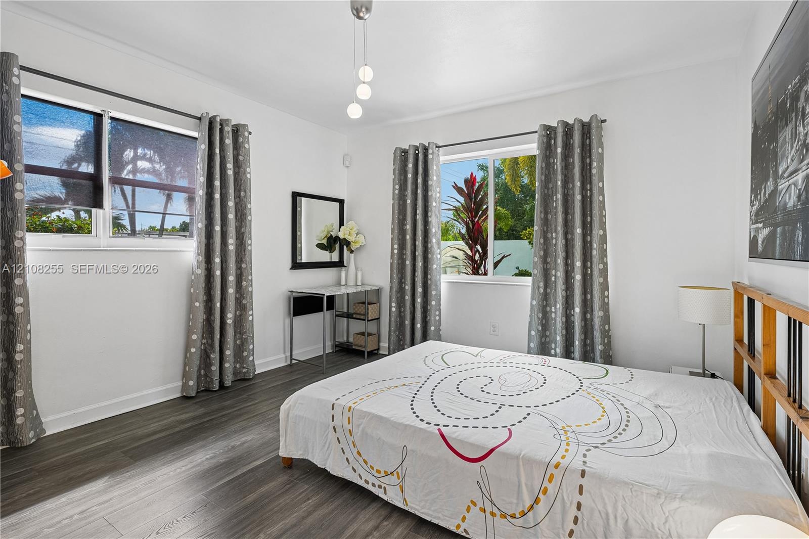 Bedroom featuring wood-finish flooring, dual windows, and a multi-pendant light fixture