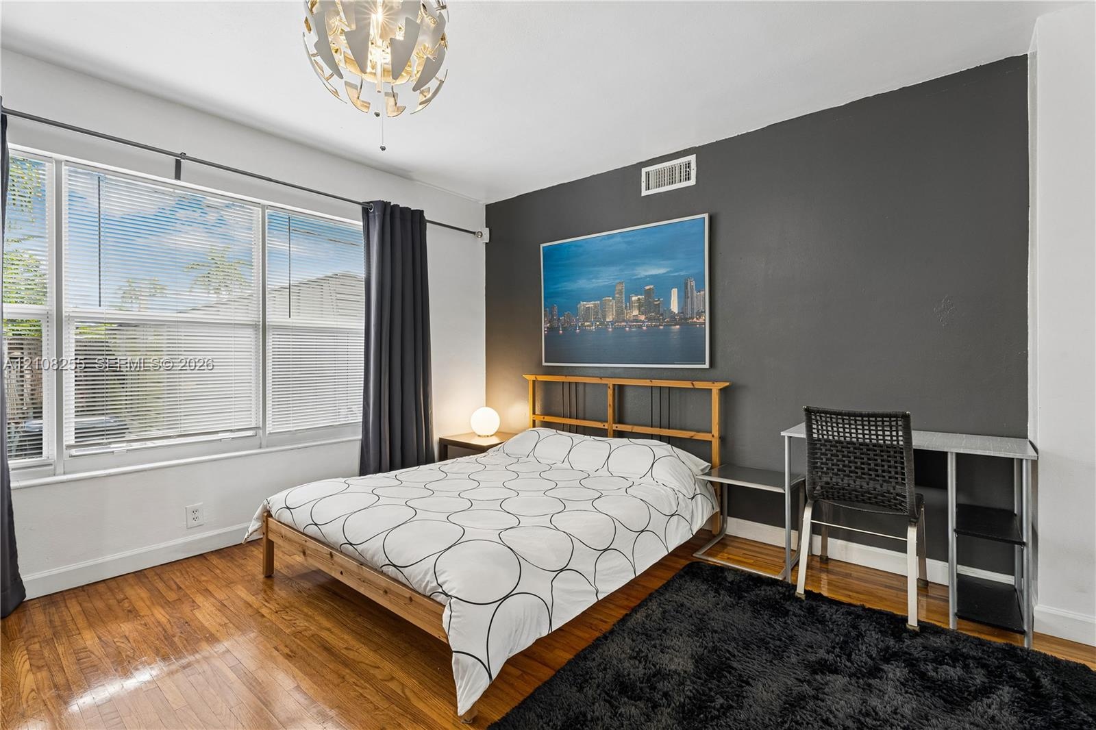 Room featuring wood-finish flooring, a charcoal accent wall, a large window with blinds, and a contemporary spherical chandelier