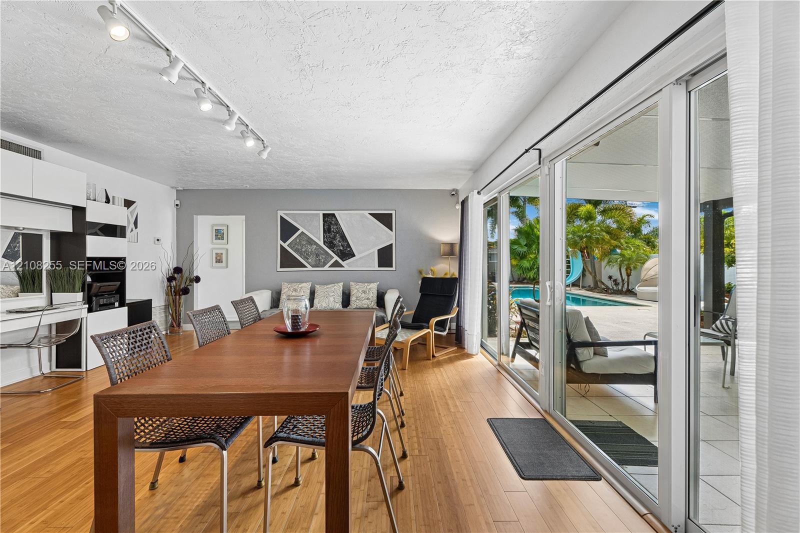 Living area featuring wood-finish flooring, built-in cabinetry, ceiling-mounted track lighting, and expansive sliding glass doors providing access to 