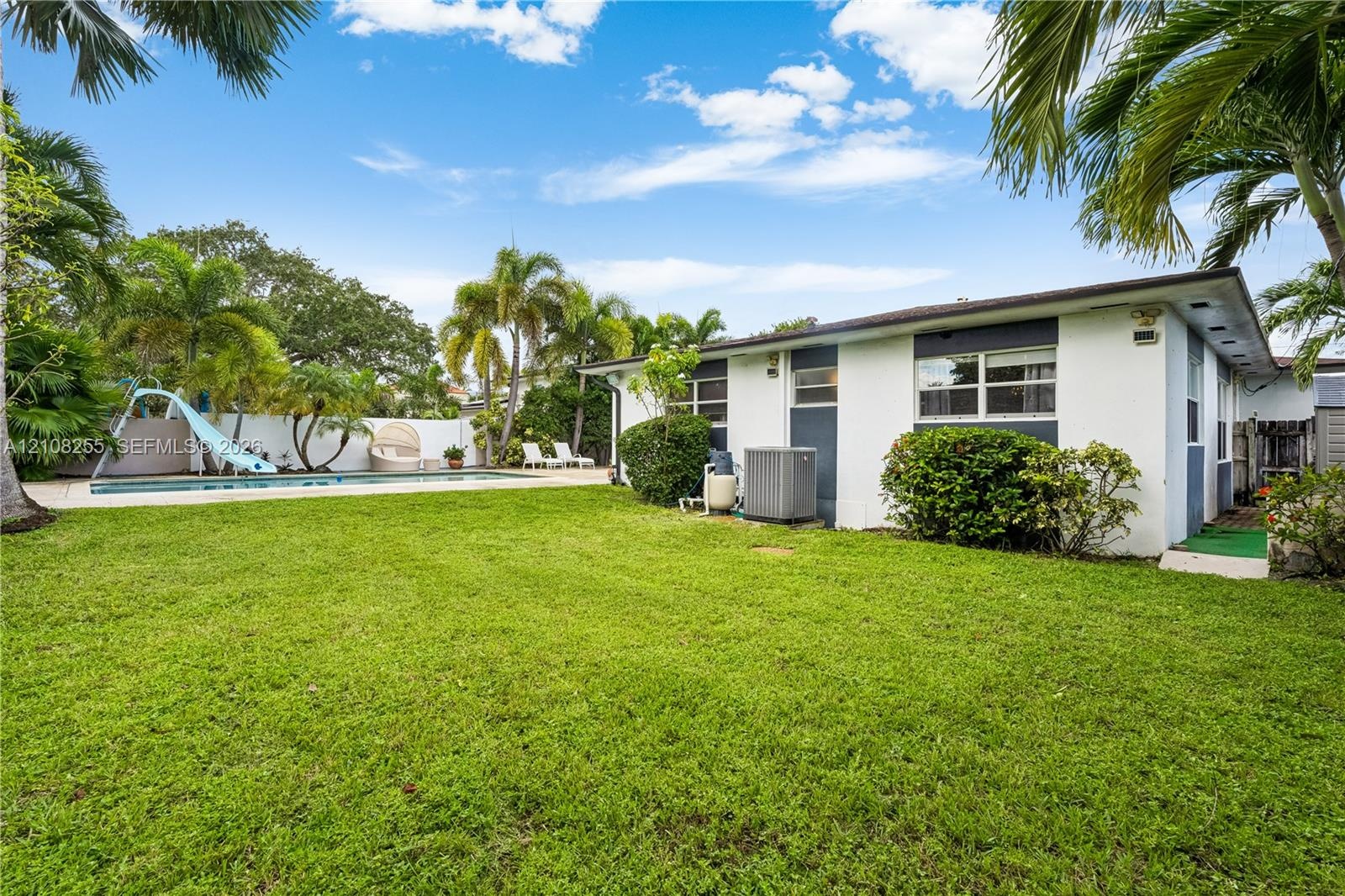 Expansive backyard featuring a rectangular swimming pool with a slide, masonry perimeter wall, mature palm trees, and manicured lawn