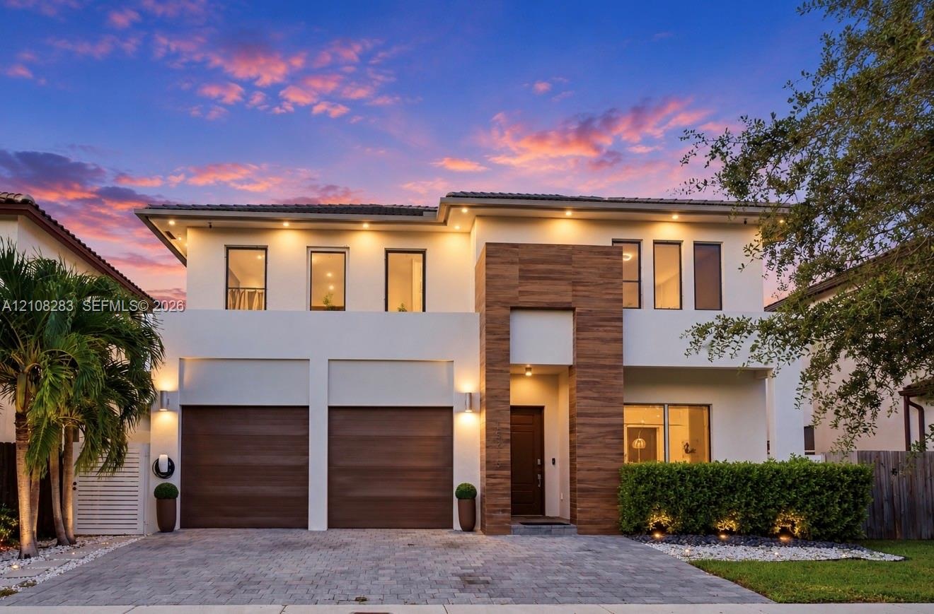 Two-story contemporary exterior featuring stucco siding, vertical wood-finish accents, dual-car garage, recessed exterior lighting, and a paved stone 