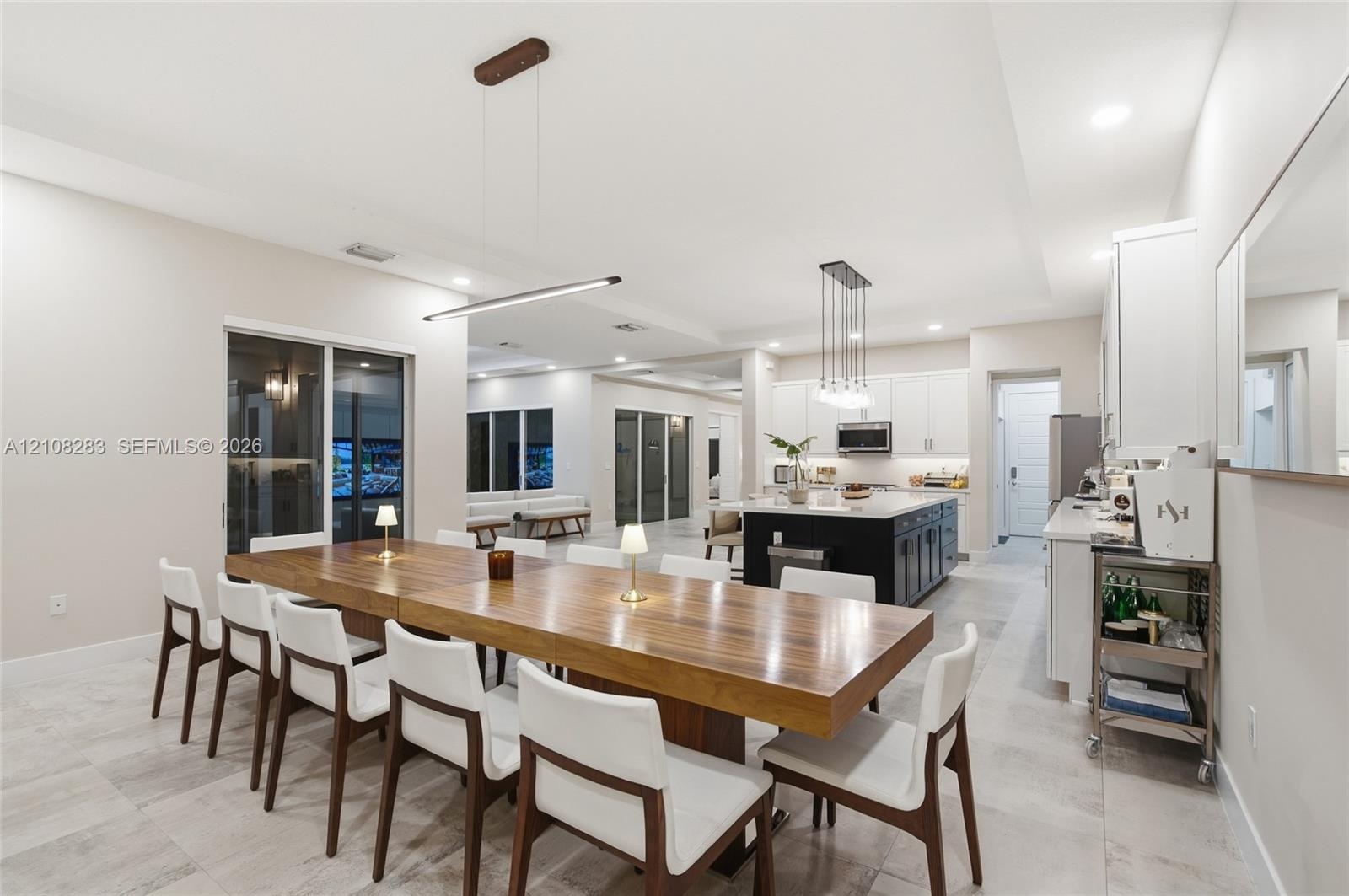 Open concept kitchen and dining area featuring large format tile flooring, a central kitchen island with contrasting cabinetry, white shaker-style wal