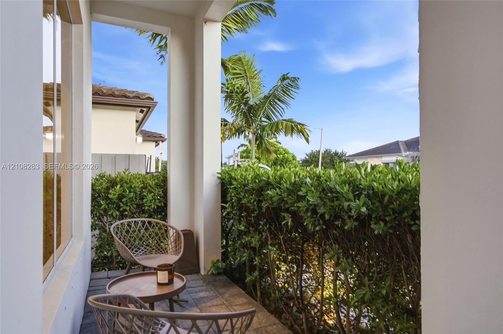 Covered patio featuring stone-tile flooring, structural support columns, and dense, manicured privacy hedging