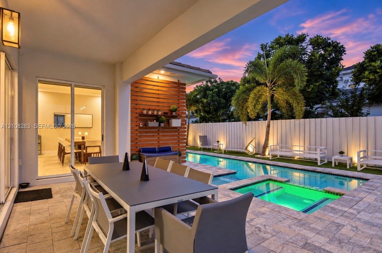 Covered patio with paver flooring, horizontal slat wood accent wall, built-in shelving, swimming pool with integrated spa, and vertical privacy fencin
