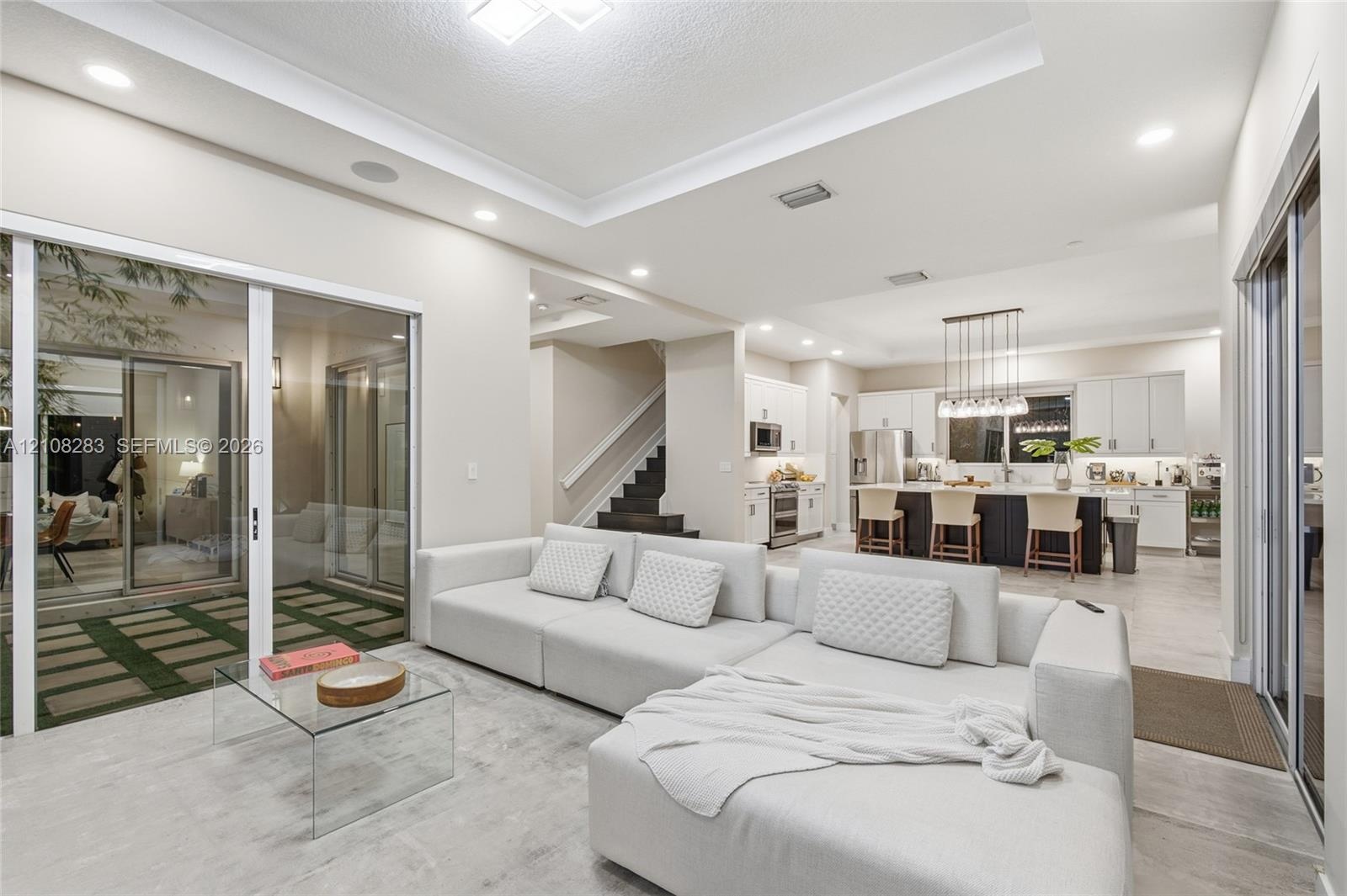 Open-concept living space featuring a tray ceiling, recessed lighting, large sliding glass doors, neutral tile flooring, and a kitchen with an oversiz