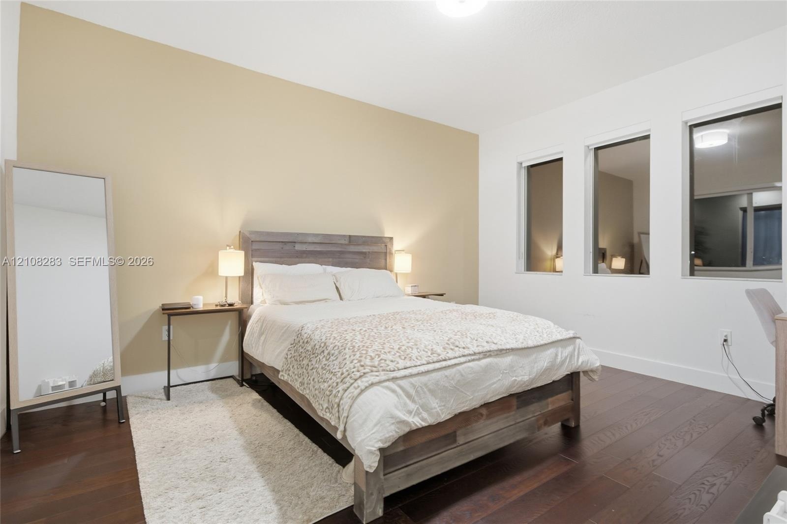 Room featuring wood-finish flooring, three vertical windows, and a neutral-toned accent wall