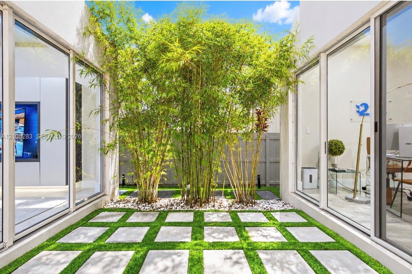 Interior courtyard featuring floor-to-ceiling glass sliding doors, concrete paver grid, synthetic turf, mature bamboo, and perimeter privacy fencing