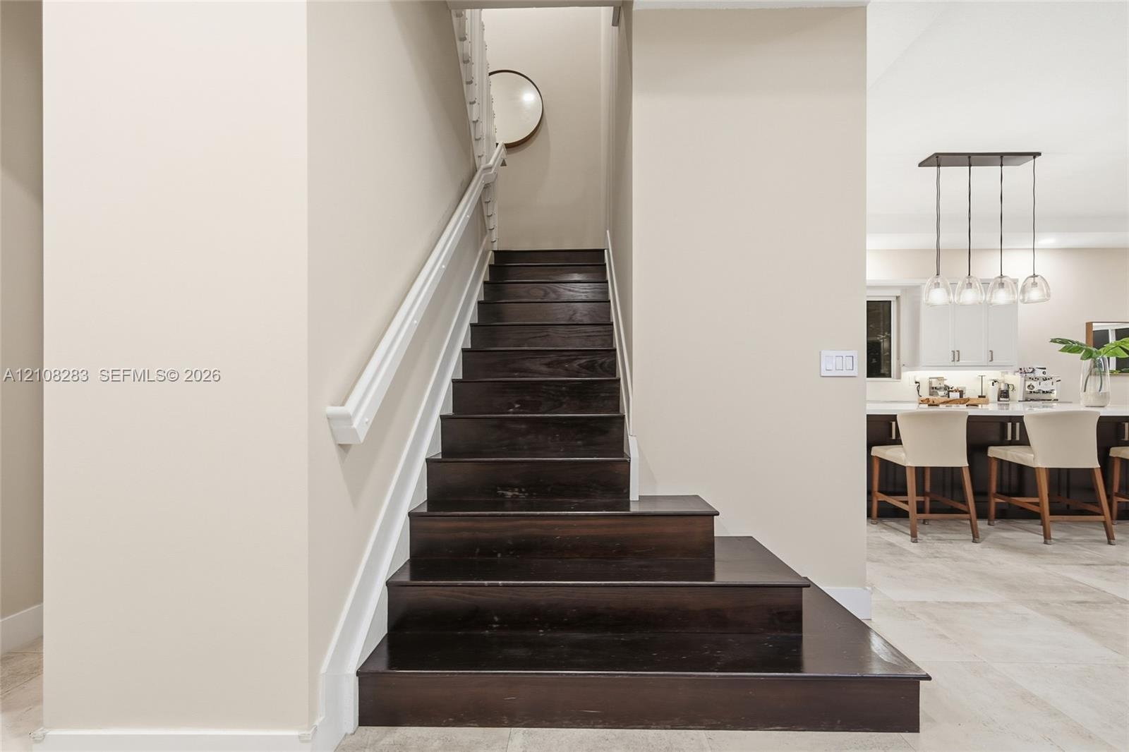 Staircase featuring dark wood-finish treads, white handrail, and white balusters, situated on stone-finish flooring with a multi-pendant light fixture