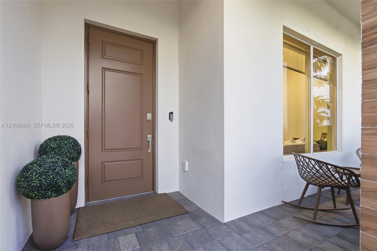 Covered entryway featuring a solid-panel door, stone paver flooring, recessed exterior lighting, and a large picture window