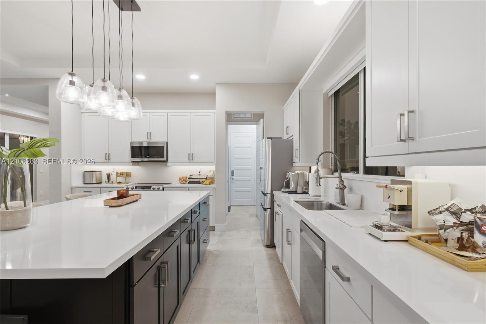 Kitchen featuring a central island with a solid-surface countertop, white shaker-style cabinetry, stainless steel appliances, and multi-light pendant 